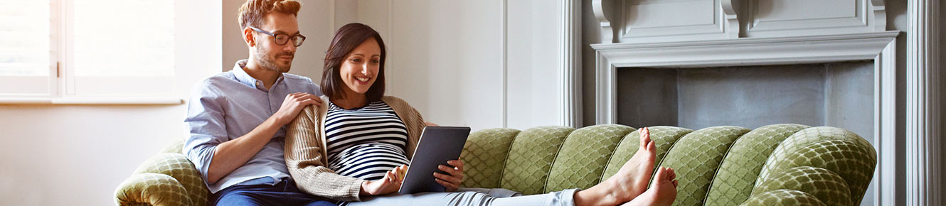 Young couple using tablet relaxing on couch at home.